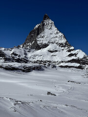 Winter view of the iconic Matterhorn peak covered in snow under a clear blue sky in the Swiss Alps. High-resolution mountain landscape ideal for travel, nature and winter sports themes.
