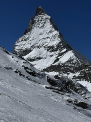 Winter view of the iconic Matterhorn peak covered in snow under a clear blue sky in the Swiss Alps. High-resolution mountain landscape ideal for travel, nature and winter sports themes.