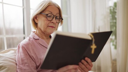 Focused senior female reading Bible in bed, spirituality and relaxation