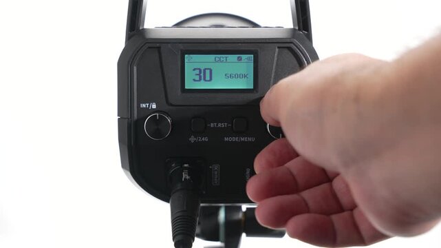 A close-up of a hand adjusting the settings of an LED studio light on the rear control panel. The display shows the CCT value as the color temperature and brightness change.