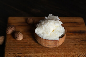 Cutting board with bowl of shea butter and nuts on wooden table