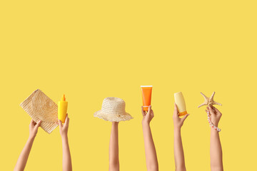 Female hands with beach accessories and hat on yellow background