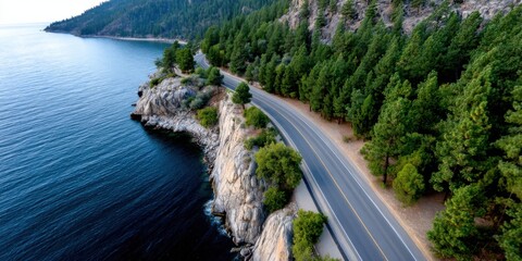 Aerial view of a cliffside highway bordered by a rocky shore and dense pine forest at dusk. 