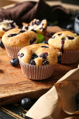 Wooden tray with tasty blueberry muffins on black wooden background, closeup