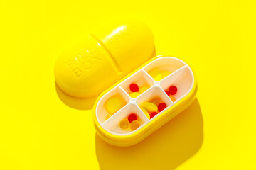 Plastic container with pills on yellow background. Top view