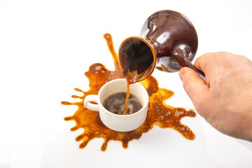 A hand pours rich coffee from a traditional ceramic pot into a white cup, creating a dramatic spill with splashes on a pristine white background, capturing the essence of a morning mishap.