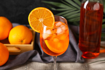 Glass of Aperol spritz cocktail with fruits and palm leaf on grey tile table