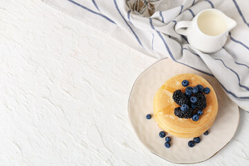 Plate of sweet pancakes with fresh blueberries, blackberries and jug of milk on white background