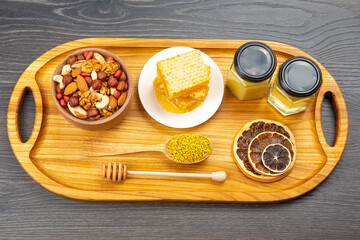 assortment of nuts and assorted dried citrus fruits and fresh floral honeycomb honey and pollen on kitchen wooden board. useful vitamin food for the human body