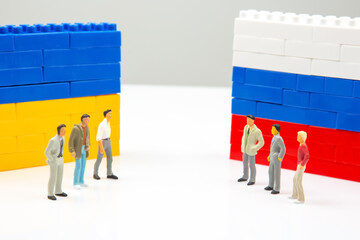 A striking image of tiny figures divided by blocks block walls in Ukrainian and Russian flag patterns, captured on a minimalist white surface.