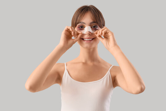 Beautiful young happy woman with bandaged nose on grey background. Plastic surgery concept
