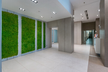 A contemporary office lobby showcases a green moss wall, polished floors, and modern lighting. The space is bright, clean, and inviting, perfect for a professional setting.