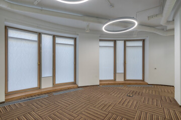 Bright office space features large windows allowing natural light, with stylish circular lighting fixtures and patterned flooring.