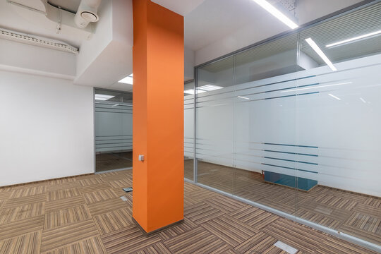 Bright and spacious office area featuring large glass walls, an orange accent wall, and a modern wooden floor design.