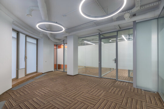 Modern office area featuring large windows, unique circular lights, and a minimalist layout. The space is bright and open, ideal for creative work or meetings.