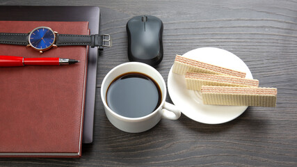 white cup of black coffee with cookies on the office table next to the laptop and clock. business and breakfast time.