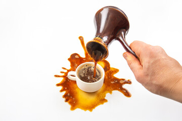 A close-up of a hand pouring coffee from a classic pot into a cup, with a messy spill forming an artistic pattern on the white background, highlighting a chaotic coffee break.