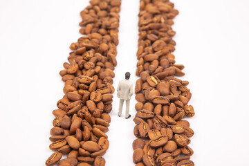A metaphorical stock shot of a small figure in a suit between coffee beans, representing determination in the coffee business. White background.