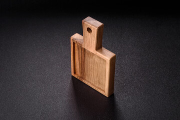 Wood, a wooden empty cutting board on a dark kitchen table. Wooden cutting board