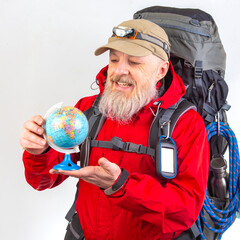 An elderly man with a white beard, wearing a red jacket and beige cap with a headlamp, holds a small globe while carrying a large backpack, isolated on a white background.