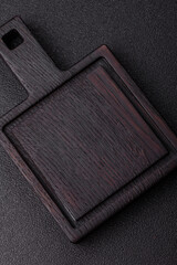 Wood, a wooden empty cutting board on a dark kitchen table. Wooden cutting board