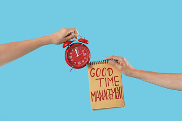 Female hands holding alarm clock and notebook with text GOOD TIME MANAGEMENT on blue background