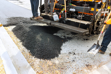 Construction workers are applying new asphalt to fix section of city street, ensuring better road quality. © ungvar
