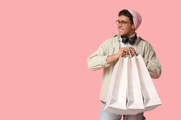 Stylish young man with shopping bags on pink background