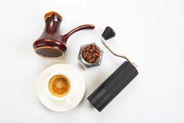 sleek black coffee grinder, a traditional ceramic cezve, a jar of coffee beans, and a white cup with fresh coffee, all on a clean white surface.
