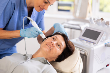 Aged female patient receiving facial radiofrequency procedure stimulating collagen production...