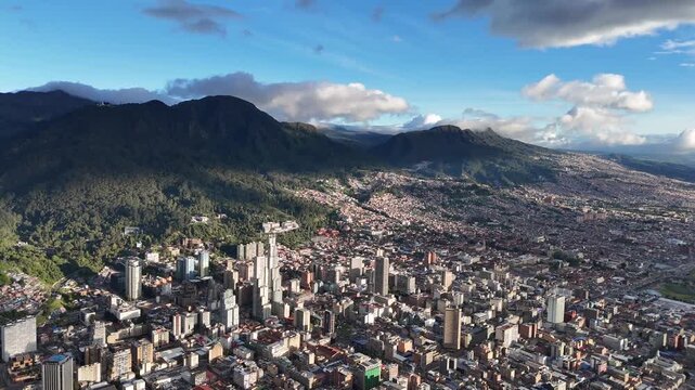Dynamic aerial view panning right toward the sun setting over the bustling urban landscape of Bogot&aacute;, Colombia, with the majestic Andes mountains in the background
