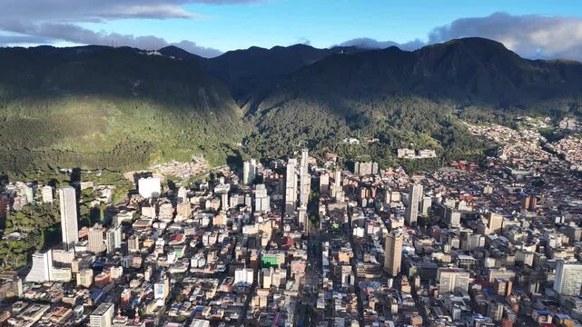A high-altitude, wide-angle drone shot pulls back to reveal the sprawling urban landscape of downtown Bogota, Colombia, with the Andes mountains in the background