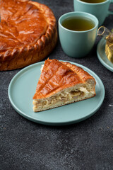 A delightful slice of golden pie rests on a soft blue plate near two cups of green tea. The inviting aroma fills a cozy kitchen, perfect for sharing with friends