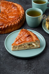 Golden brown pie sits on a pale blue plate, showcasing its flaky crust and filling. Two cups of tea rest nearby, inviting warmth and comfort. Perfect for a cozy afternoon