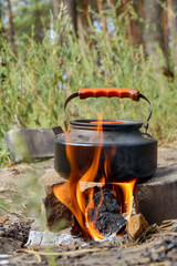 black camping kettle heating on fire in nature, vertical frame