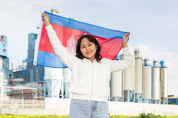Cheerful asian girl with cambodian flag standing in front of factory