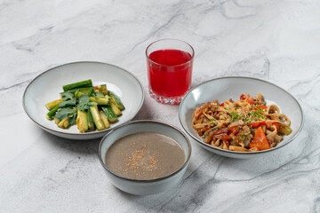 A vibrant meal features three dishes: sautéed vegetables, savory noodles topped with herbs, and a rich sauce, all accompanied by a refreshing red drink