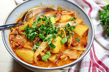 Hearty stew made from cabbage, potatoes, chorizo sausage and tomatoes in a bowl with parsley garnish, warming meal in autumn or winter time, selected focus