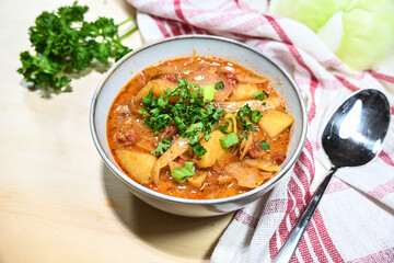 Cabbage soup or stew with chorizo sausage, potatoes, and tomatoes in a bowl with parsley garnish, hearty homemade meal for autumn or winter time, copy space, selected focus
