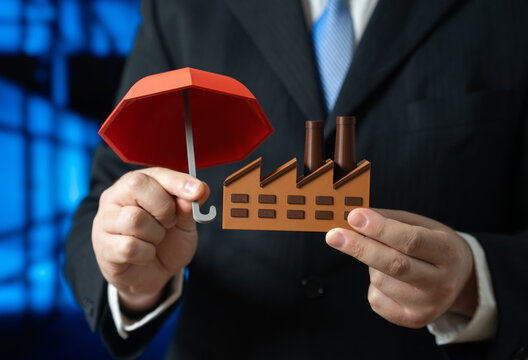 A businessman insures his factory with an umbrella. Insurance in industry. Protection of assets and risk management. Industrial safety, business continuity and corporate security policies. - Powered by Adobe