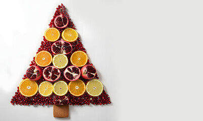 Creative fruit Christmas tree with pomegranates, apples, citrus, rosemary, and dried orange slices, styled for a warm festive atmosphere