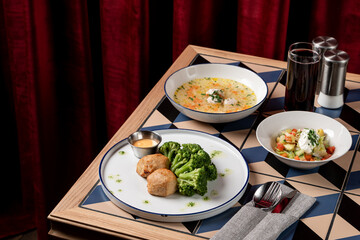 A mouthwatering meal is displayed on a stylish table with a geometric design. The plate features broccoli and dumplings, accompanied by soup and a fresh salad, creating a delightful dining experience