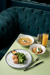 Enjoying a diverse meal with a creamy soup, fresh vegetables, and a refreshing drink at a charming diner. The atmosphere is inviting and warm