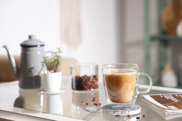 Glass cup of cappuccino with coaster and coffee beans on table in room, closeup