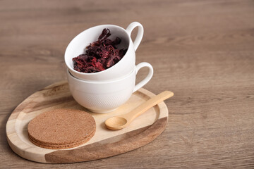 Cups with dry hibiscus tea, coaster and spoon on table in kitchen