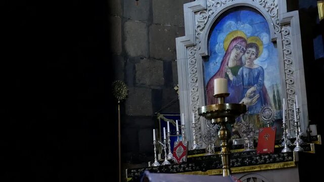 interior view of a stone church featuring a painting of Jesus Christ on the wall. Below stands a stone baptismal font and a red ceremonial stand.