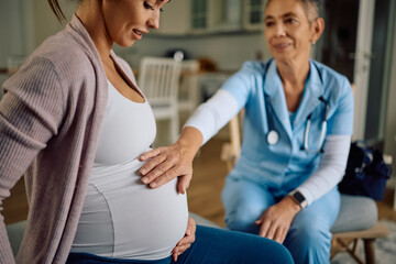 Close up of obstetrician nurse touching pregnant woman's belly during a home visit.