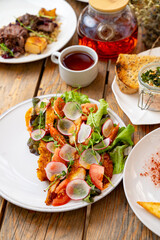 A colorful salad featuring crisp lettuce, ripe tomatoes, and sliced radishes rests on a rustic wooden table. Nearby, a steaming cup of tea and hearty side dishes create a cozy dining atmosphere
