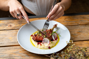A diner engages with a beautifully plated dish, carefully slicing into a succulent piece of meat atop a creamy base. The atmosphere is warm and inviting, perfect for relaxation