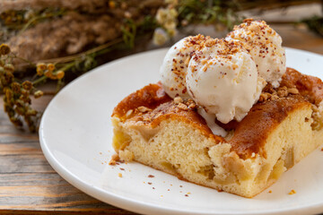 A warm slice of peach cobbler rests on a white plate, adorned with scoops of ice cream and a sprinkle of crushed nuts. The scene is cozy and inviting, perfect for dessert lovers